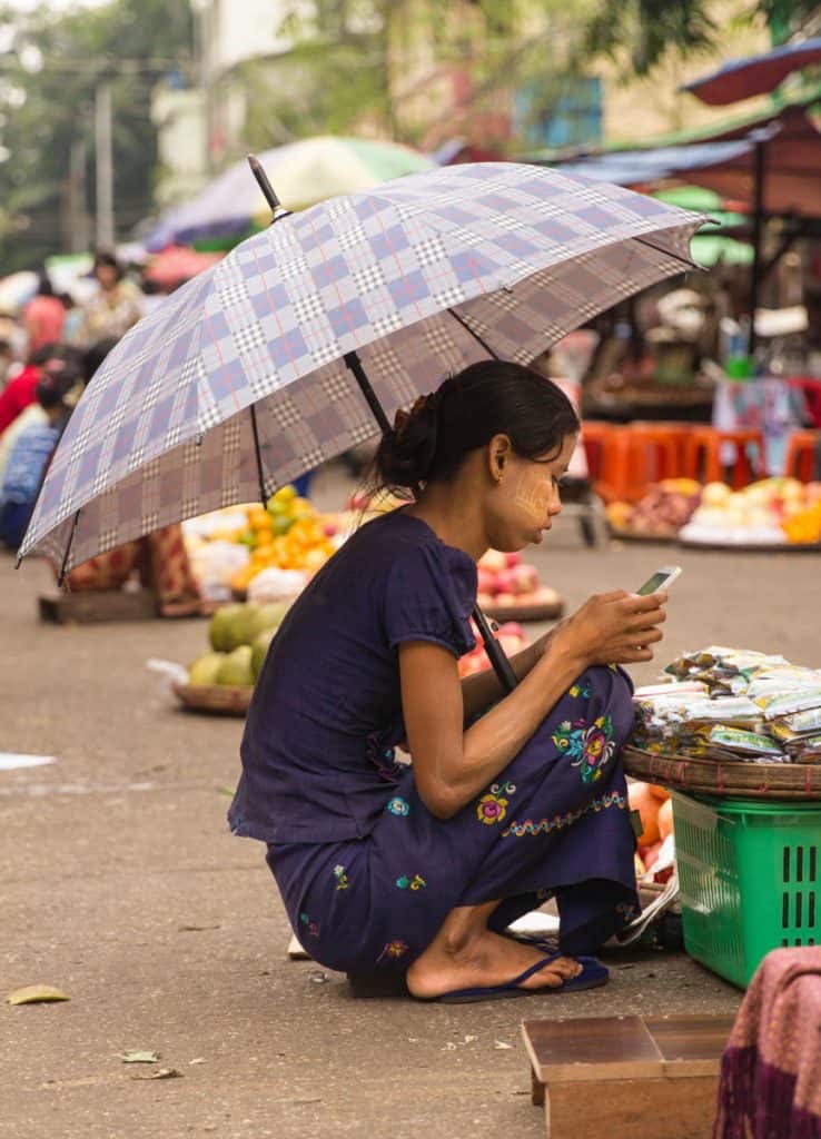 Burmese girl playing with her phone in the middle of market