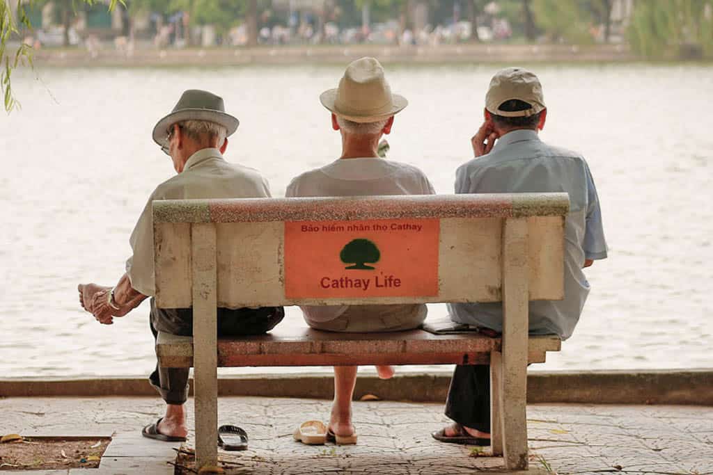 Three older man sitting on a bench and looking at Hanoi's lake