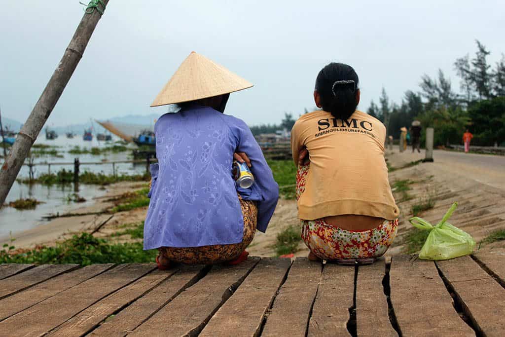 the backs of two Vietnamese women sitting on the dock