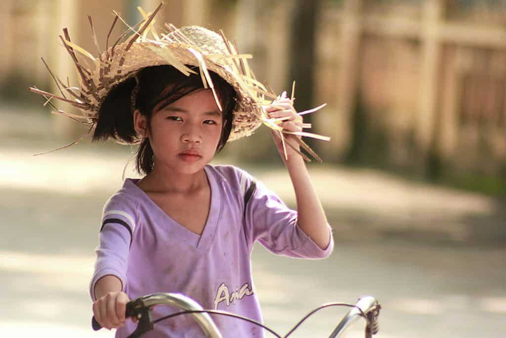 Vietnamese girl riding a bike and holding a straw hat