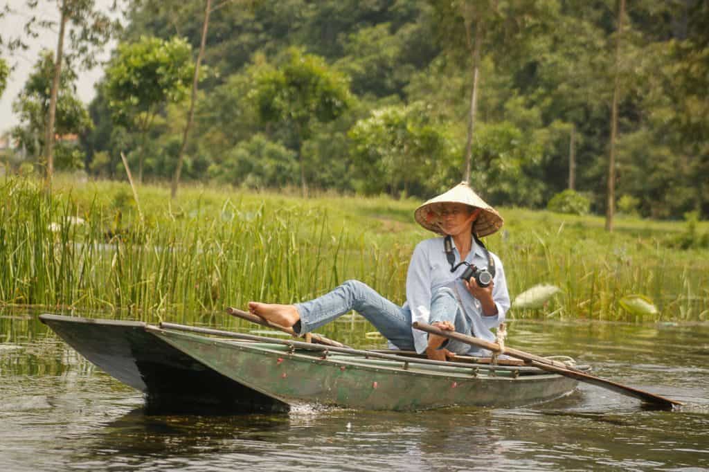 One of the rowers in Ninh Binh rowing the boat with her feet while holding a camera