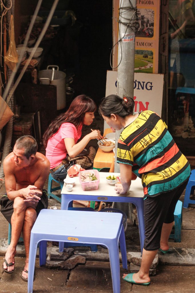 Peaople eating on sidewalk in one of Hanoi's food stands