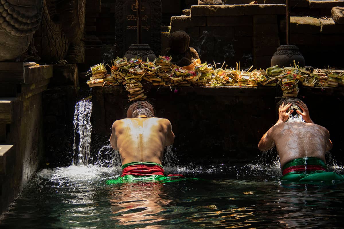 men taking a dip in the holy water temple in bali